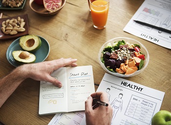 hands writing in a health journal on a table surrounded by healthy foods